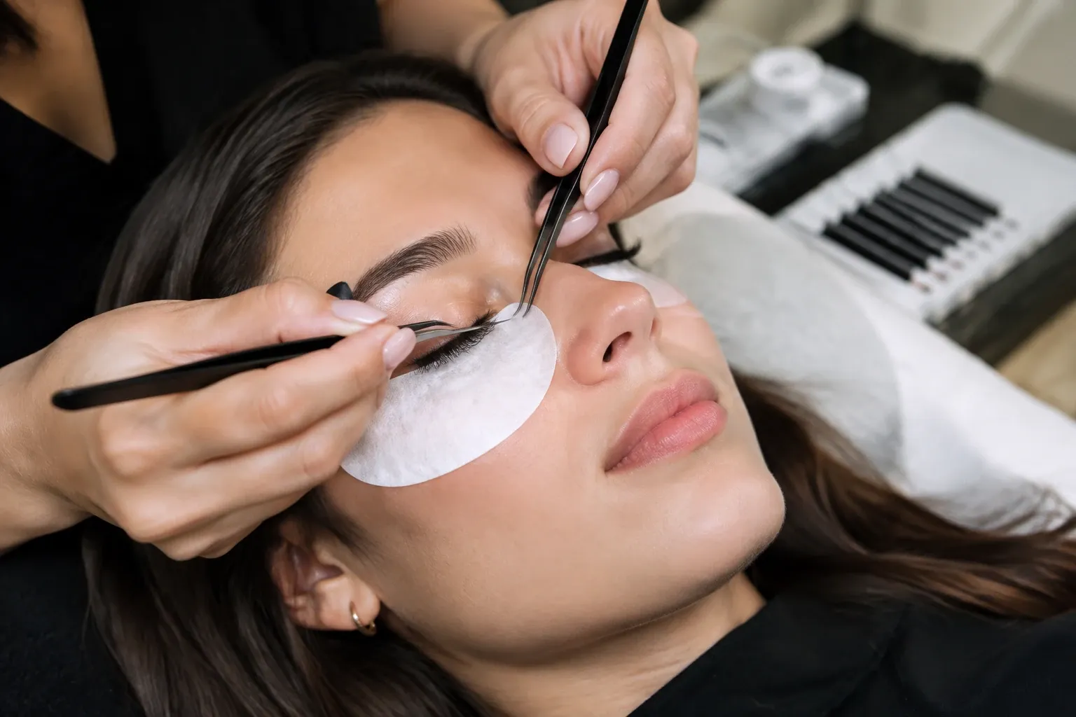 Vrouw liggend met oogpads terwijl stylist individuele wimperextensions aanbrengt